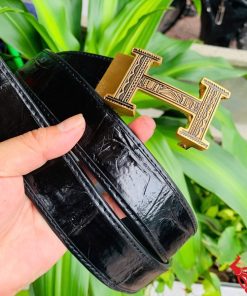 Hình ảnh thắt lưng TSK103 màu đen, da cá sấu cao cấp, đầu khóa ray thép không gỉ, cầm trên tay trước nền cây xanh.