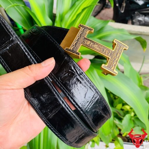 Hình ảnh thắt lưng TSK103 màu đen, da cá sấu cao cấp, đầu khóa ray thép không gỉ, cầm trên tay trước nền cây xanh.