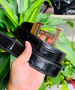 Hình ảnh thắt lưng TSK103 màu đen, da cá sấu cao cấp, đầu khóa ray thép không gỉ, cầm trên tay với cây xanh và mô tô phía sau.