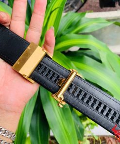 Hình ảnh thắt lưng TSK103 màu đen, da cá sấu sang trọng, đầu khóa ray thép không gỉ, cầm trên tay với cây xanh phía sau.