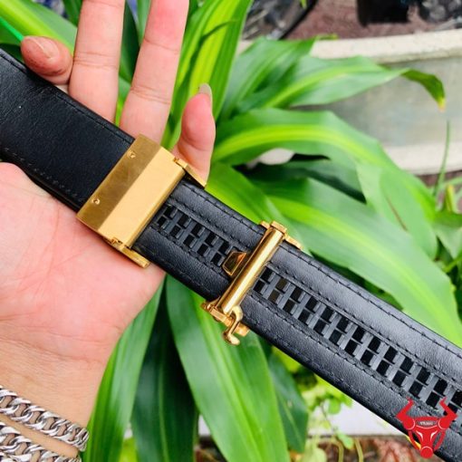 Hình ảnh thắt lưng TSK103 màu đen, da cá sấu sang trọng, đầu khóa ray thép không gỉ, cầm trên tay với cây xanh phía sau.