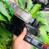 Hình ảnh thắt lưng da cá sấu TSK32 màu đen, mặt khóa lăn inox cao cấp, được cầm trên tay trước nền cây xanh và mô tô.