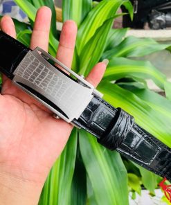 Hình ảnh thắt lưng TSK32 màu đen, da cá sấu cao cấp, mặt khóa lăn inox, cầm trên tay trước nền cây xanh.