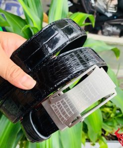 Hình ảnh thắt lưng TSK32 màu đen, da cá sấu cao cấp, mặt khóa lăn inox, cầm trên tay với cây xanh và mô tô phía sau.