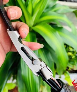 Hình ảnh thắt lưng TSK32 màu đen, da cá sấu sang trọng, mặt khóa lăn inox, cầm trên tay với cây xanh phía sau.