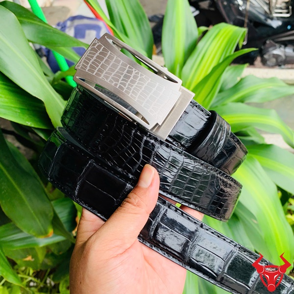 Thời trang cao cấp - Thắt Lưng Da Cá Sấu TSK32 Hình ảnh thắt lưng da cá sấu TSK32 màu đen, mặt khóa lăn inox cao cấp, được cầm trên tay trước nền cây xanh và mô tô.