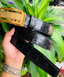 Hình ảnh thắt lưng TSK33 màu đen, da cá sấu cao cấp, khóa tỳ thép vàng, cầm trên tay trước nền cây xanh.