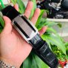 Hình ảnh thắt lưng da cá sấu TSK33 màu đen, khóa tỳ thép trắng cao cấp, được cầm trên tay trước nền cây xanh rực rỡ.