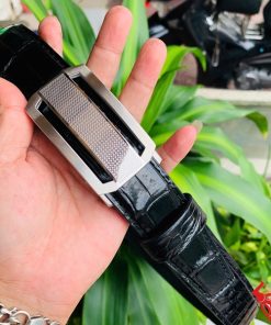 Hình ảnh thắt lưng da cá sấu TSK33 màu đen, khóa tỳ thép trắng cao cấp, được cầm trên tay trước nền cây xanh rực rỡ.