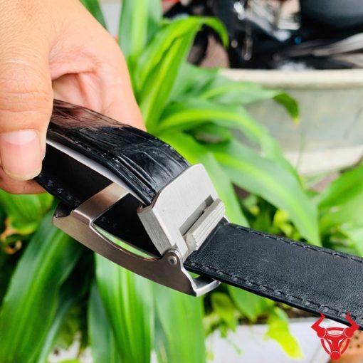 Hình ảnh thắt lưng TSK33 màu đen, da cá sấu sang trọng, khóa tỳ thép trắng, cầm trên tay với nền cây xanh.