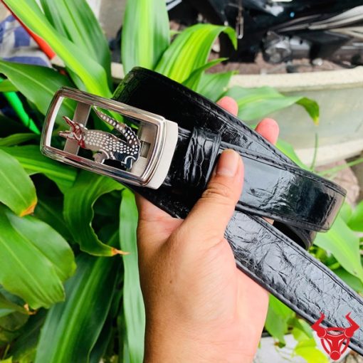 Hình ảnh thắt lưng TSK73 màu đen, da cá sấu sang trọng, mặt khóa ray trượt inox, cầm trên tay với nền cây xanh và mô tô.