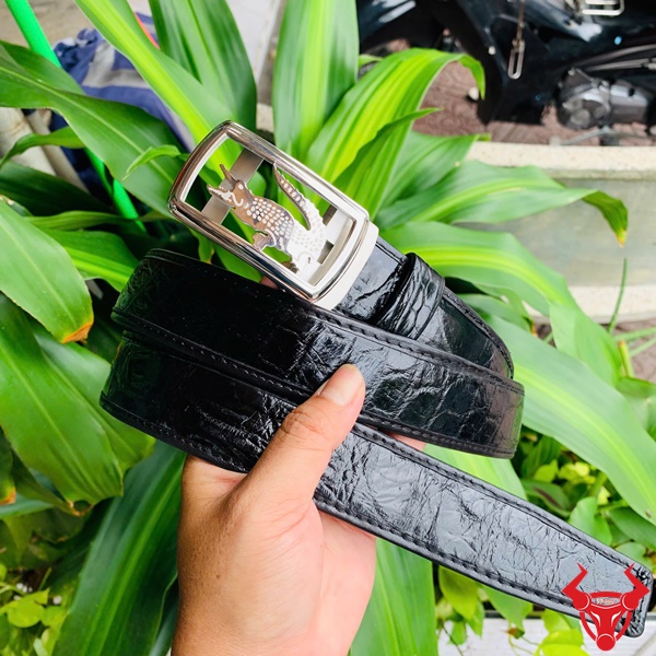 Phong cách thời thượng - Thắt Lưng TSK73 Hình ảnh thắt lưng TSK73 màu đen, da cá sấu cao cấp, mặt khóa ray trượt inox, cầm trên tay với cây xanh và mô tô phía sau.