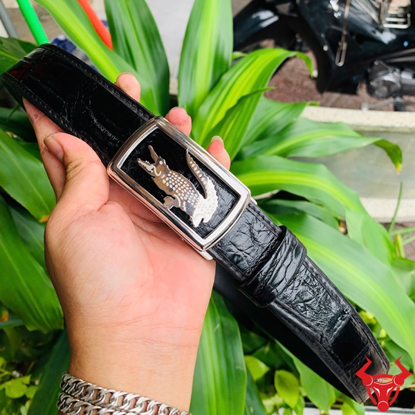 Thời trang cao cấp - Thắt Lưng Da Cá Sấu TSK73 Hình ảnh thắt lưng da cá sấu TSK73 màu đen, mặt khóa ray trượt inox với họa tiết cá sấu, được cầm trên tay trước nền cây xanh rực rỡ.