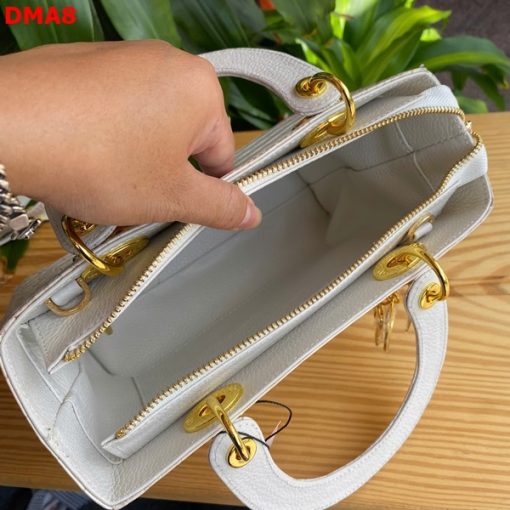 Hình ảnh túi xách TDA8 màu bạch tạng, da bụng cá sấu cao cấp, khóa vàng nổi bật, đặt trên bàn gỗ với cây xanh và mô tô.