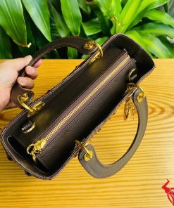 Hình ảnh túi xách TDA4 màu nâu đất, da cá sấu cao cấp, khóa vàng nổi bật, đặt trên bàn gỗ với cây xanh và mô tô.