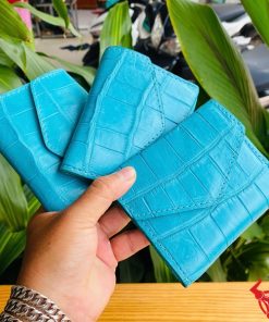 Ba chiếc ví nữ 3 gấp mini da bụng cá sấu VRAA8 xanh dương trong tay, nền lá cây, đại diện cho sự thời trang, phong cách và nhỏ gọn.
