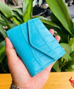 Ba chiếc ví 3 gấp mini da cá sấu VRAA8 màu turquoise trong tay, nền xanh, đại diện sự thời trang, phong cách nhỏ gọn.