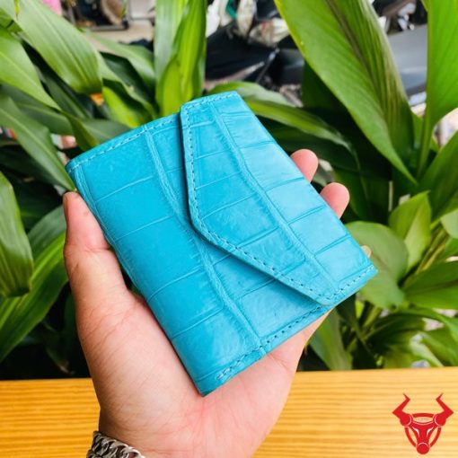 Ba chiếc ví 3 gấp mini da cá sấu VRAA8 màu turquoise trong tay, nền xanh, đại diện sự thời trang, phong cách nhỏ gọn.