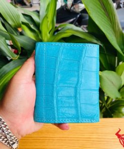 Hình ảnh cầm ba ví nữ VRAA8 da bụng cá sấu 3 gấp mini xanh dương, nền thực vật, thể hiện thời trang, phong cách và nhỏ gọn.