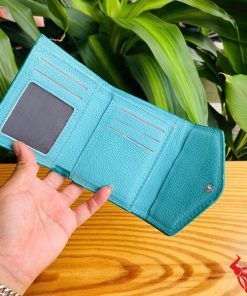 Ba chiếc ví nữ 3 gấp mini da bụng cá sấu VRAA8 màu xanh dương cầm trên tay, nền lá cây xanh, nhấn mạnh sự thời trang, phong cách và nhỏ gọn cho sản phẩm.
