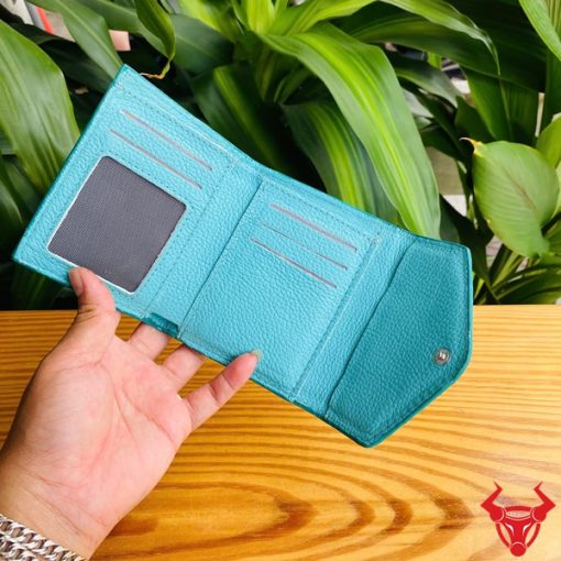 Ba chiếc ví nữ 3 gấp mini da bụng cá sấu VRAA8 màu xanh dương cầm trên tay, nền lá cây xanh, nhấn mạnh sự thời trang, phong cách và nhỏ gọn cho sản phẩm.
