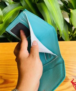 Hình ảnh cầm ba ví mini da cá sấu VRAA8 3 gấp màu xanh, nền thực vật tươi mát, đại diện cho thời trang, phong cách nhỏ gọn và hấp dẫn.