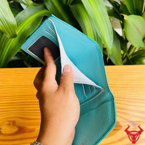 Hình ảnh cầm ba ví mini da cá sấu VRAA8 3 gấp màu xanh, nền thực vật tươi mát, đại diện cho thời trang, phong cách nhỏ gọn và hấp dẫn.